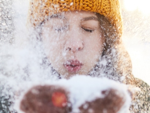 Frau mit oranger Mütze pustet Schnee in Kamera